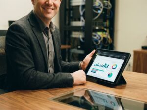 Professional businessperson at desk viewing colorful Power BI dashboard on tablet with IT servers in background