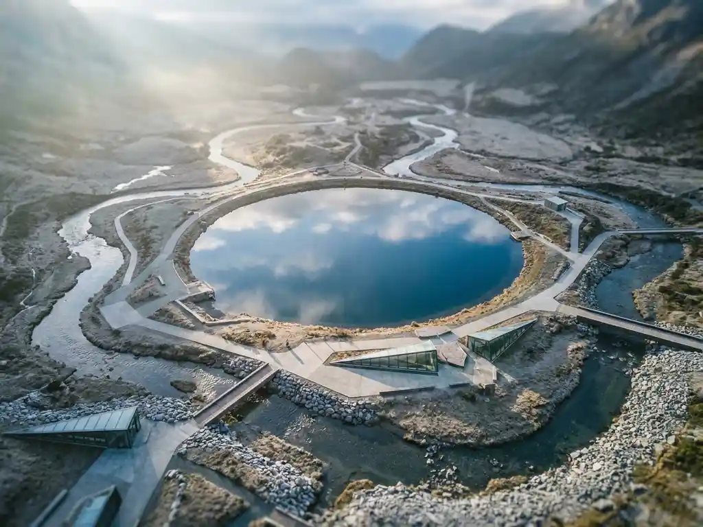 Luchtfoto van een saffierblauwe bergmeer met meerdere toestromende rivieren, omgeven door een modern landschap in zacht ochtendlicht.